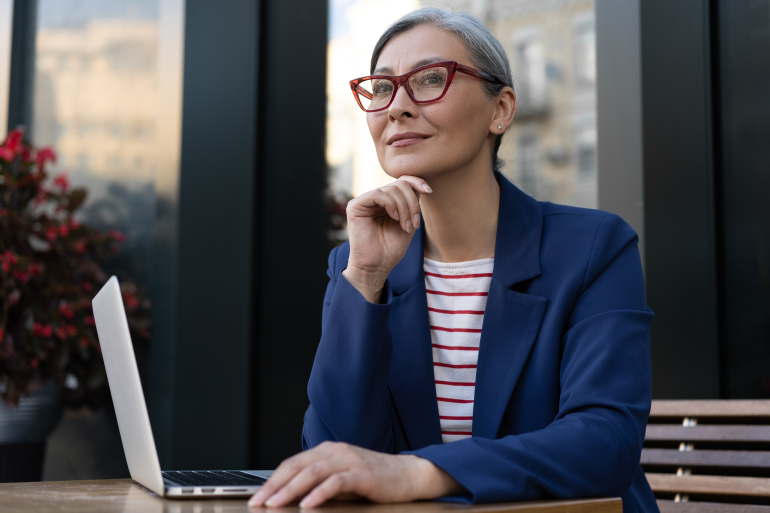 Lady with glasses pondering with laptop in front of her