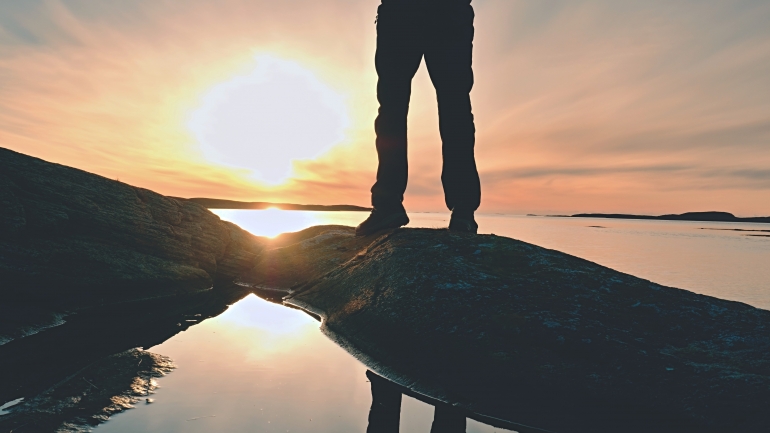 Man hiker figure stand on rock peak, sea with sunset sun