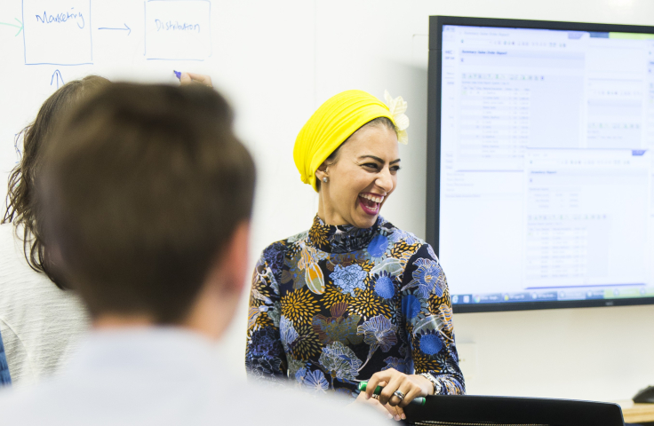 a smiling woman teaches in front of a whiteboard