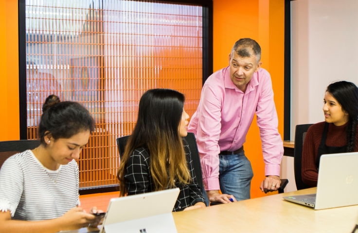 students and a teacher in a room with laptops