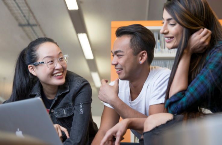 Three students using a computer, smiling and laughing together