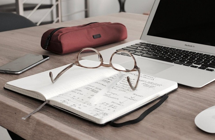 An opened notebook with written notes, and a pair of light brown glasses on it